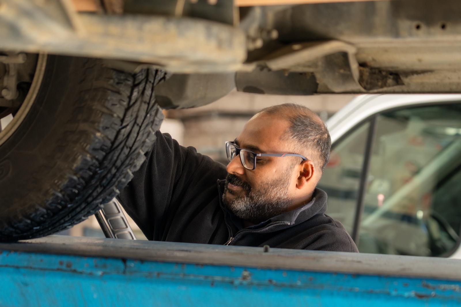 Technician inspecting the wheel hub and underbody of a vehicle raised on the workshop hoist.