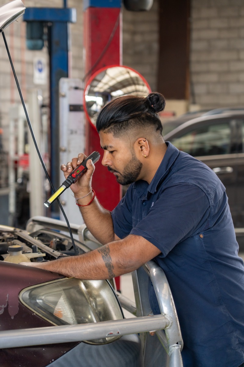 Mechanic working under the bonnet with an inspection lamp at our Frankton workshop.