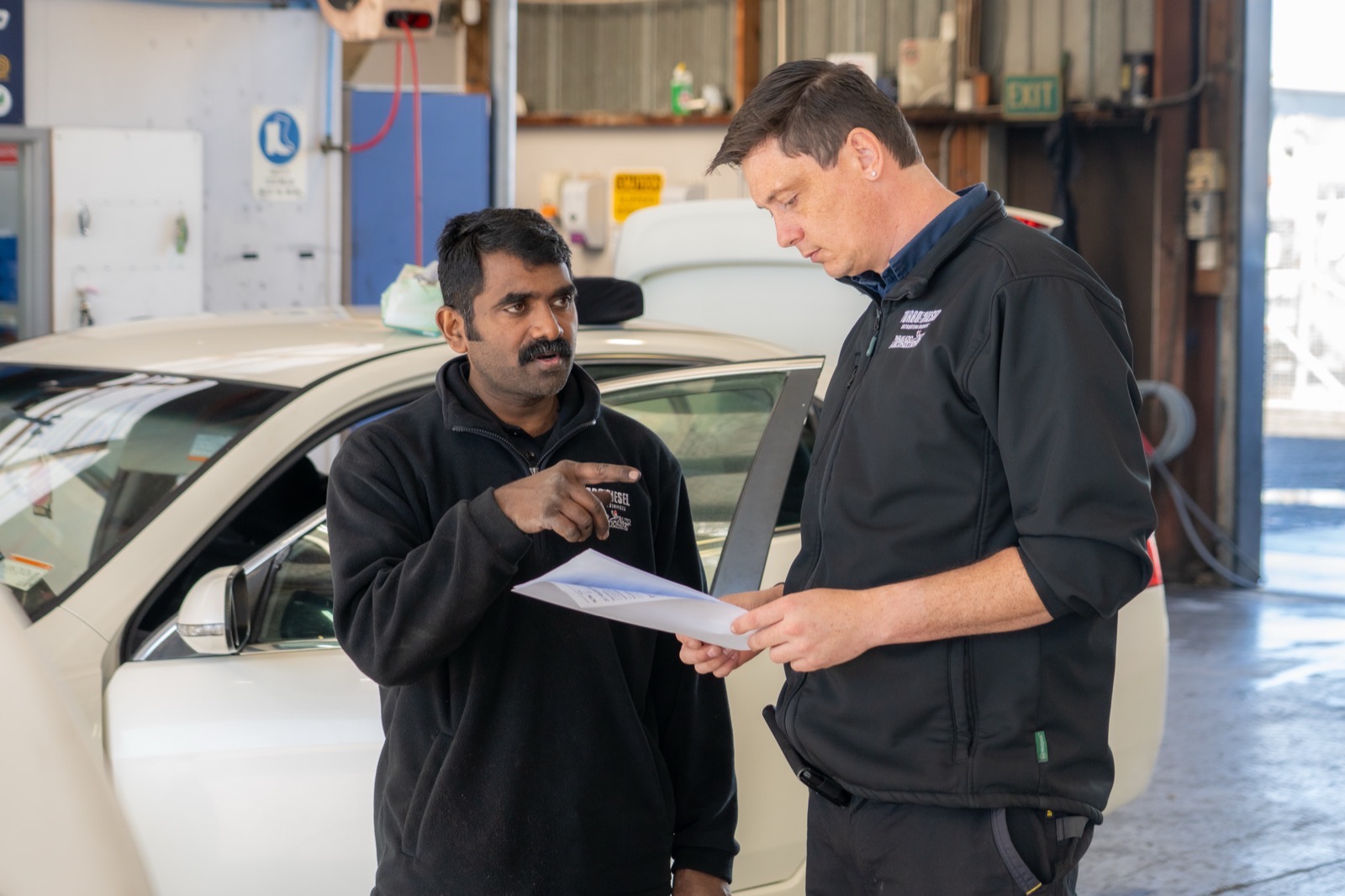 Two Turbo & Diesel staff reviewing job paperwork beside a customer vehicle.