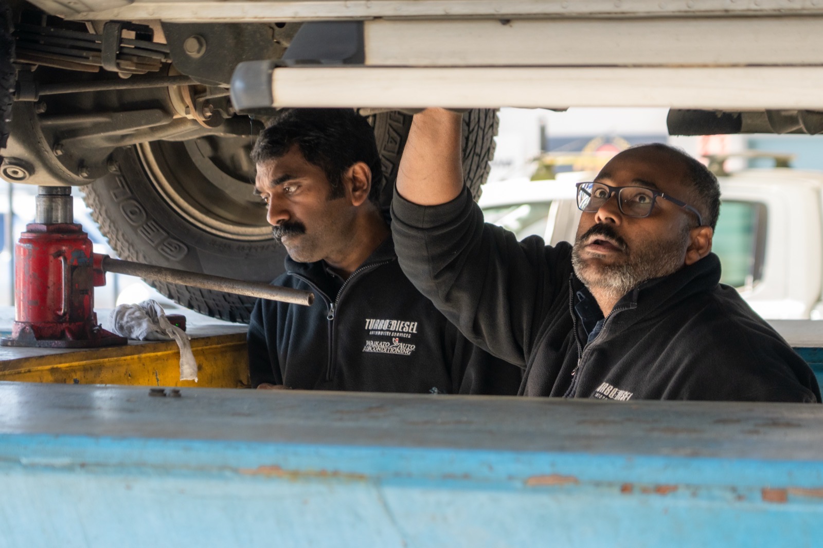 Two Turbo & Diesel technicians in branded workwear working under a raised ute together.